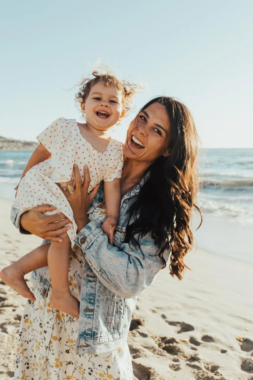 Jade laughing on the beach while holding her daughter Nova